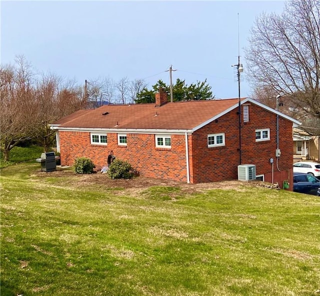 view of side of home featuring a chimney, brick siding, a yard, and central AC