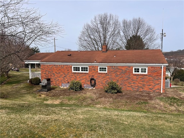 rear view of property with brick siding, a yard, and a chimney