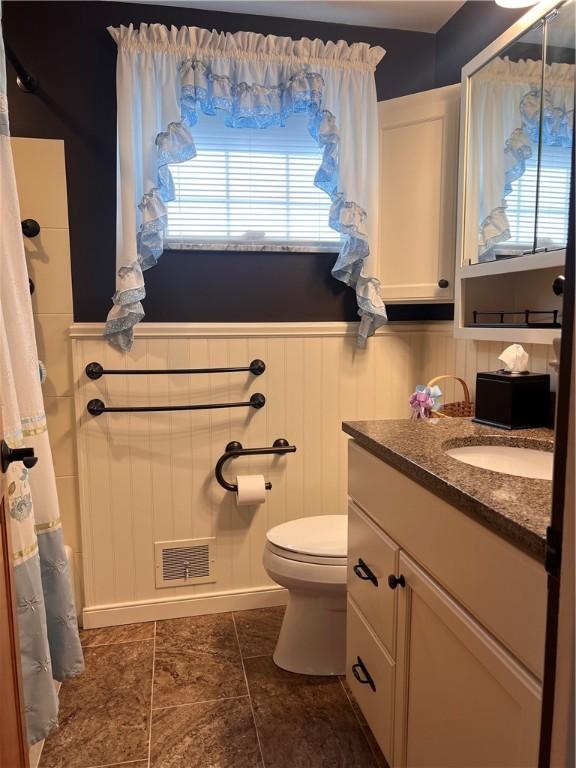 full bath featuring vanity, curtained shower, toilet, visible vents, and wainscoting