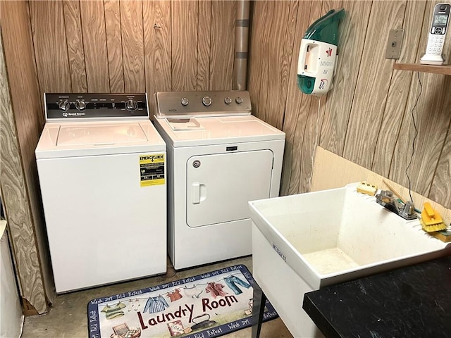 laundry area featuring wooden walls, laundry area, a sink, and washer and clothes dryer