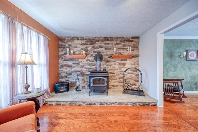 living area with a wood stove, a textured ceiling, an accent wall, and wood finished floors