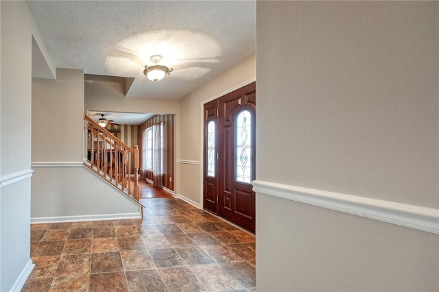 foyer featuring a ceiling fan, stairs, stone finish flooring, baseboards, and a textured ceiling