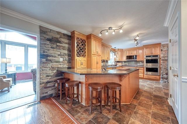 kitchen featuring appliances with stainless steel finishes, dark countertops, a peninsula, ornamental molding, and a breakfast bar area