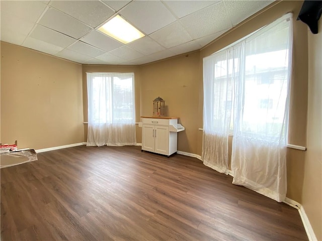 empty room featuring a paneled ceiling, dark wood finished floors, and a wealth of natural light