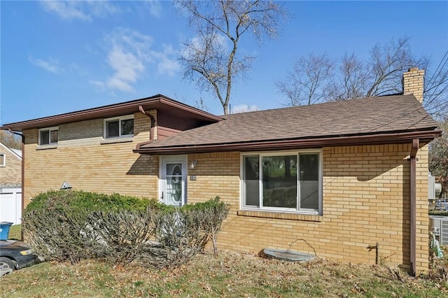view of front of house featuring a chimney, a shingled roof, and brick siding