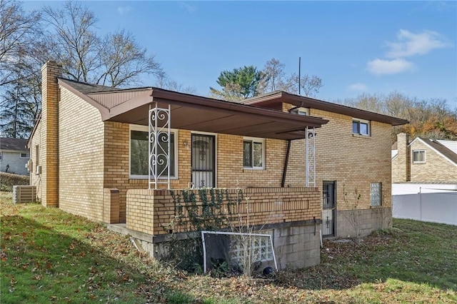 back of house featuring fence, a chimney, brick siding, a lawn, and a porch