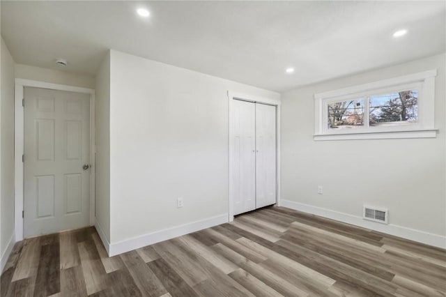 unfurnished bedroom featuring recessed lighting, baseboards, visible vents, a closet, and wood finished floors
