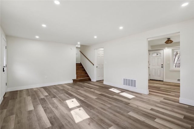 unfurnished room featuring visible vents, baseboards, wood finished floors, recessed lighting, and stairway