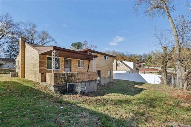 back of property with a chimney, cooling unit, fence, brick siding, and a yard