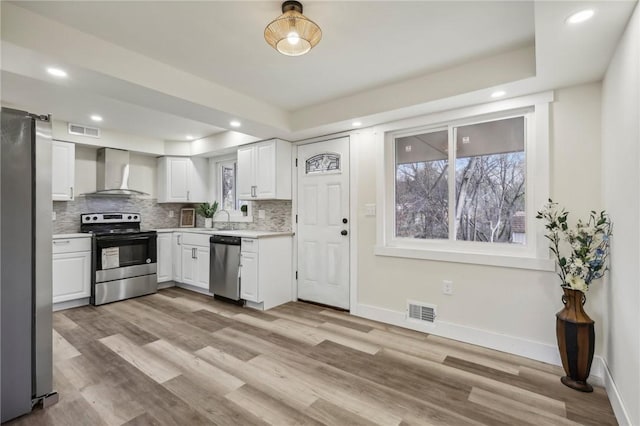 kitchen with light countertops, backsplash, white cabinets, appliances with stainless steel finishes, and wall chimney exhaust hood