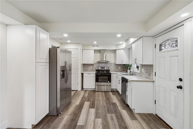 kitchen featuring light countertops, stainless steel appliances, backsplash, a sink, and wall chimney range hood