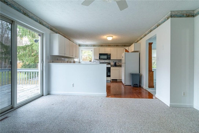 kitchen with a textured ceiling, black microwave, electric range oven, dark carpet, and freestanding refrigerator