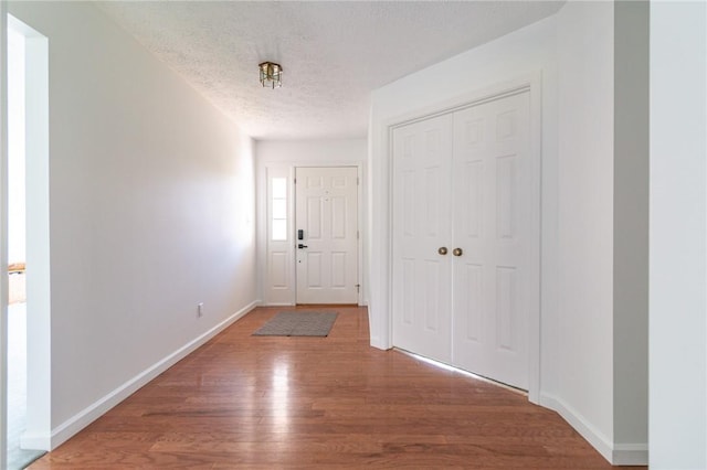 foyer entrance featuring baseboards, wood finished floors, and a textured ceiling