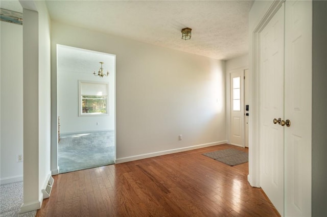 interior space featuring a textured ceiling, baseboards, visible vents, an inviting chandelier, and hardwood / wood-style flooring
