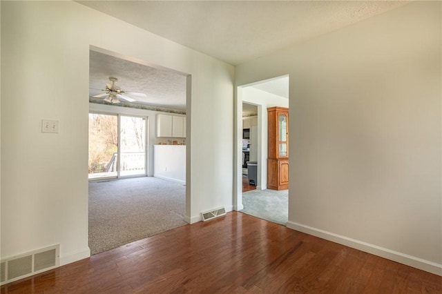 spare room featuring wood finished floors, visible vents, a ceiling fan, and baseboards