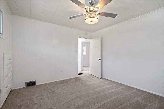 carpeted spare room with visible vents, a ceiling fan, crown molding, and baseboards