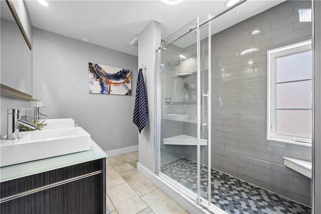 bathroom featuring baseboards, a shower stall, tile patterned floors, a sink, and double vanity