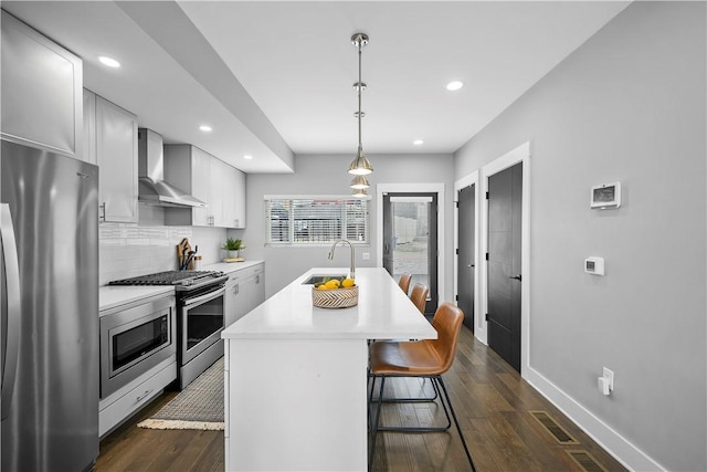 kitchen featuring light countertops, a sink, wall chimney exhaust hood, appliances with stainless steel finishes, and dark wood finished floors
