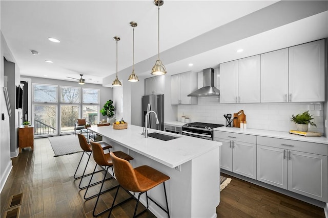 kitchen with decorative backsplash, ceiling fan, appliances with stainless steel finishes, a sink, and wall chimney range hood