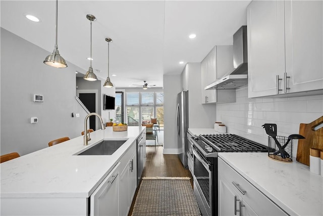 kitchen featuring a sink, a ceiling fan, appliances with stainless steel finishes, wall chimney range hood, and decorative backsplash