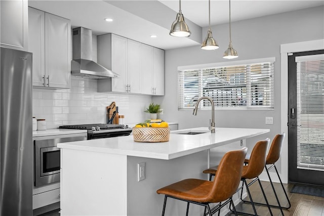 kitchen with light countertops, a sink, wall chimney range hood, backsplash, and freestanding refrigerator