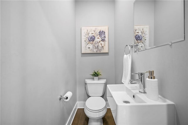bathroom with baseboards, wood finished floors, toilet, and a sink