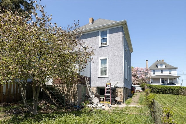 rear view of house featuring stucco siding, fence, stairway, and a chimney