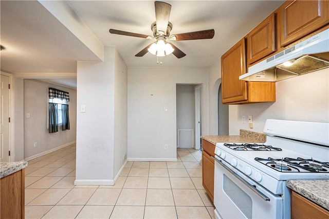 719 Zimmerman St, Jeannette, PA 15644 - kitchen with white gas range, under cabinet range hood, brown cabinetry, and light tile patterned floors