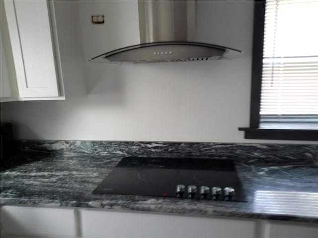 interior details featuring wall chimney exhaust hood, black electric stovetop, white cabinets, and dark countertops
