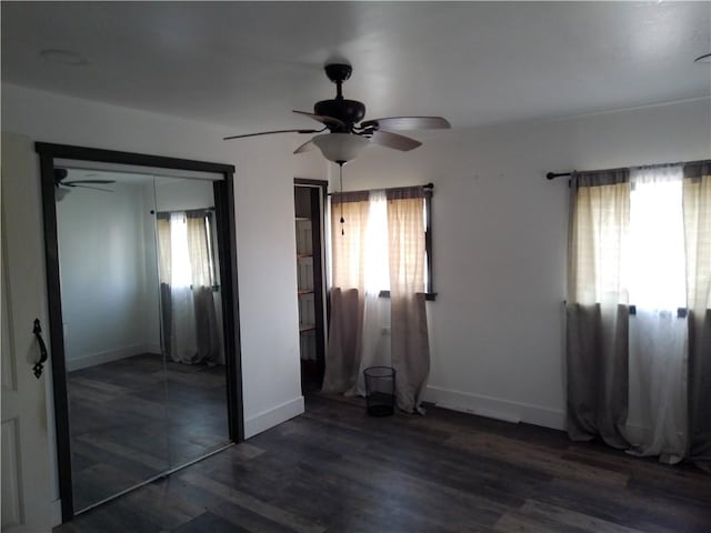 unfurnished bedroom featuring a closet, baseboards, multiple windows, and dark wood-type flooring