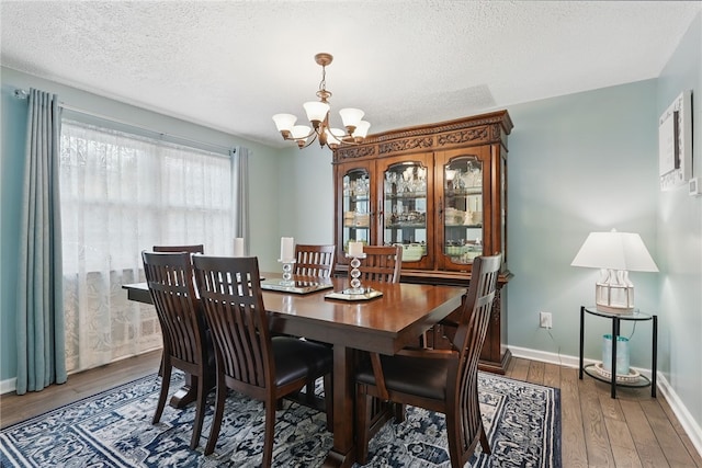 dining area featuring wood finished floors, a textured ceiling, baseboards, and an inviting chandelier