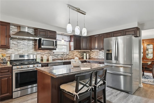 kitchen with wall chimney exhaust hood, appliances with stainless steel finishes, dark brown cabinets, and light wood-style floors