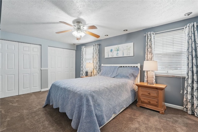carpeted bedroom with two closets, a textured ceiling, a ceiling fan, and baseboards