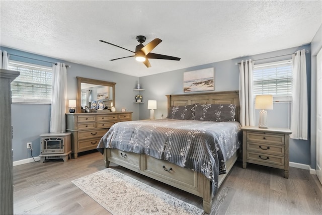 bedroom featuring baseboards, a wood stove, multiple windows, and light wood-type flooring