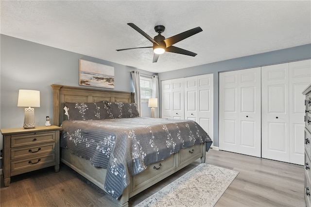 bedroom with a ceiling fan, wood finished floors, a textured ceiling, and two closets