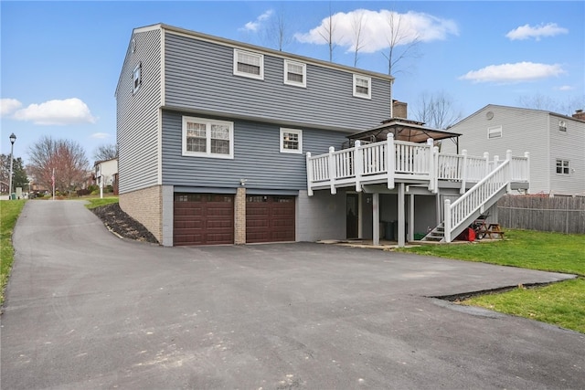 back of property with stairway, an attached garage, a wooden deck, driveway, and a gazebo