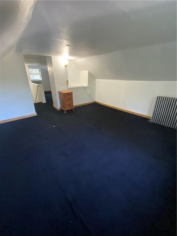additional living space with baseboards, radiator, lofted ceiling, and dark colored carpet