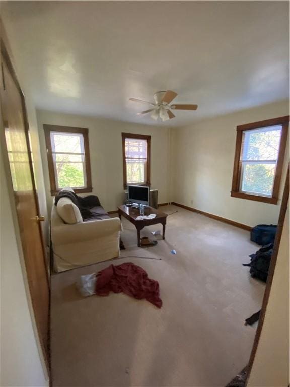 living area with baseboards, a ceiling fan, and light carpet