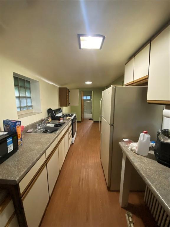 kitchen featuring white cabinets, a sink, range with gas stovetop, freestanding refrigerator, and light wood-type flooring