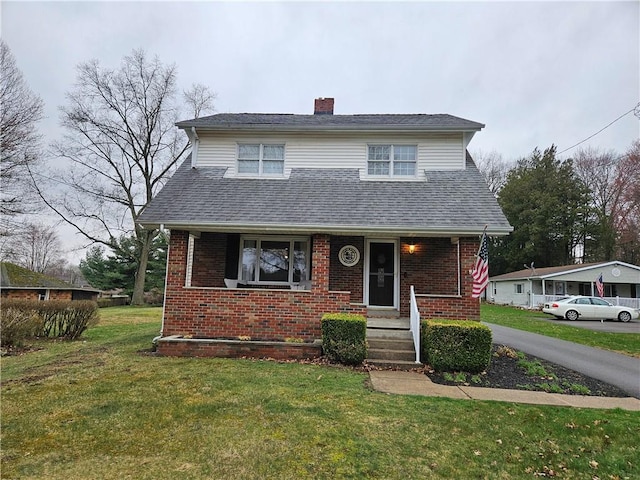 view of front facade with a chimney, brick siding, a front yard, and roof with shingles