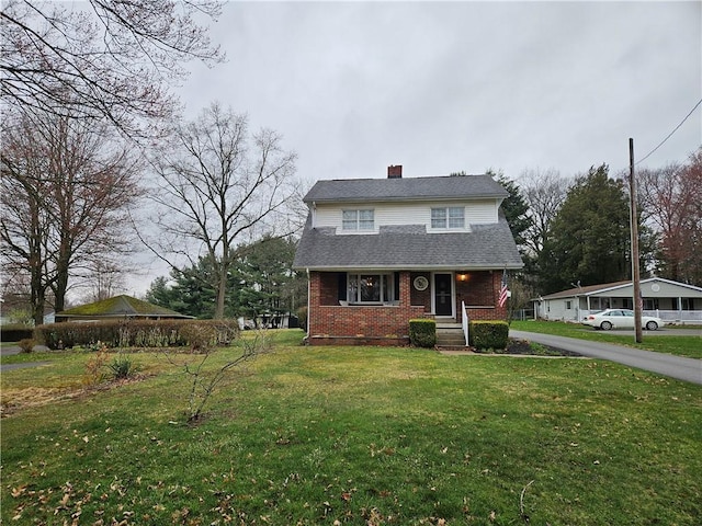 view of front of property with brick siding, a front lawn, a chimney, and roof with shingles