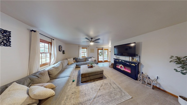 living area featuring light colored carpet, a glass covered fireplace, a ceiling fan, and baseboards