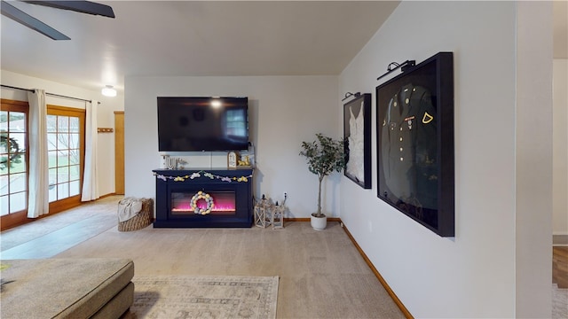 carpeted living area with a glass covered fireplace, ceiling fan, and baseboards