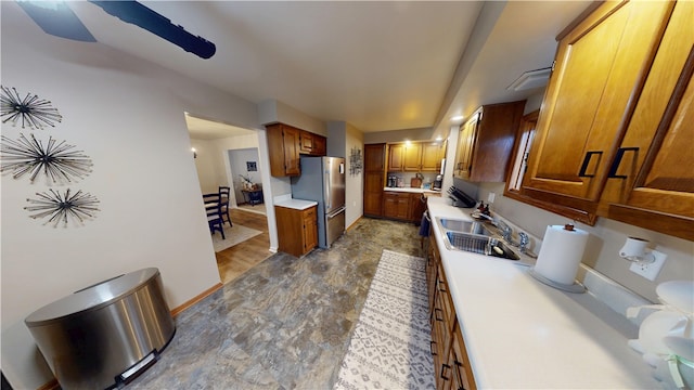 kitchen featuring freestanding refrigerator, a sink, light countertops, brown cabinets, and baseboards