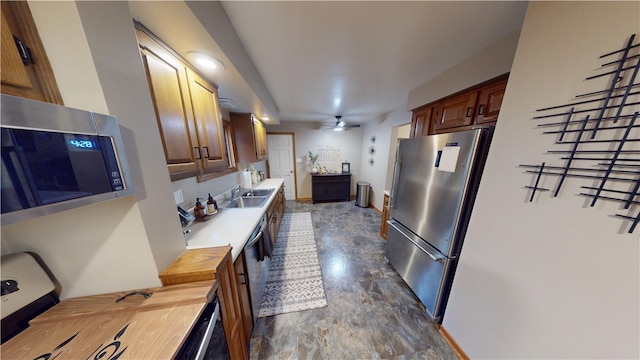 kitchen with appliances with stainless steel finishes, a sink, a ceiling fan, wooden counters, and baseboards