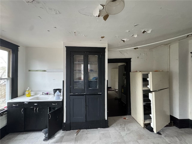 kitchen featuring a sink, glass insert cabinets, dark cabinetry, and a ceiling fan