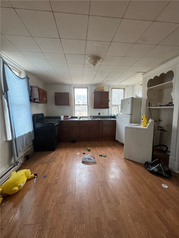 kitchen with freestanding refrigerator, wood finished floors, dark countertops, black electric range, and a sink