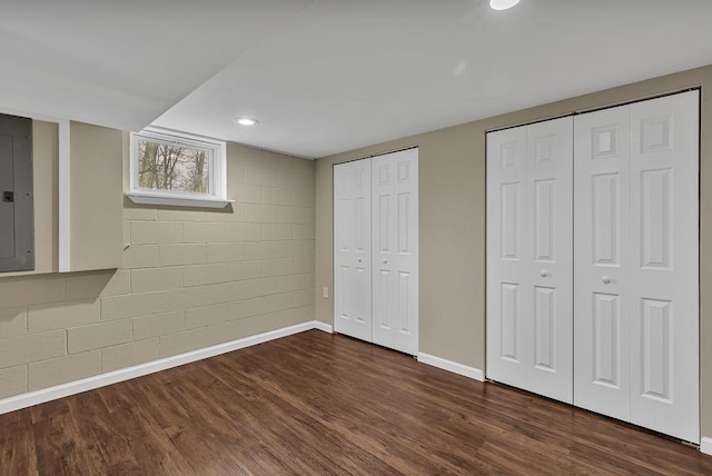 interior space with electric panel, concrete block wall, dark wood-style floors, multiple closets, and baseboards