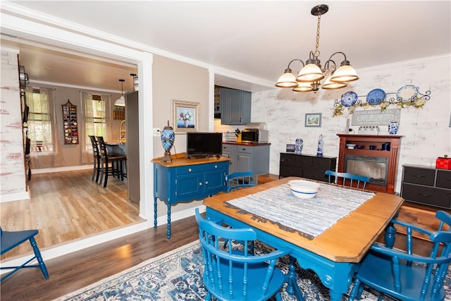 dining space featuring wood finished floors, a chandelier, baseboards, ornamental molding, and a fireplace