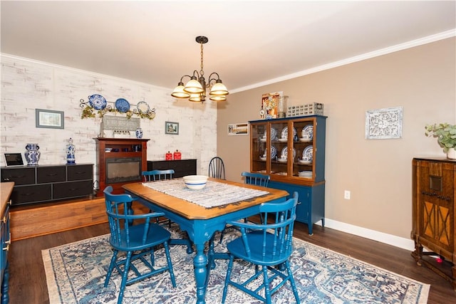 dining room with a chandelier, baseboards, wood finished floors, crown molding, and a glass covered fireplace